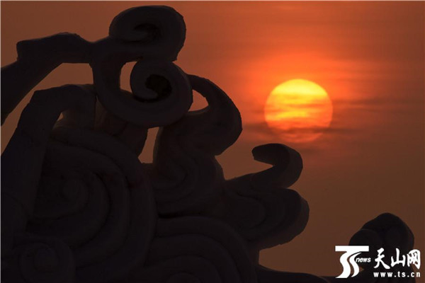 在新疆博斯騰湖大河口（西海漁村）景區，一輪紅日從雪雕“祥雲”後升起